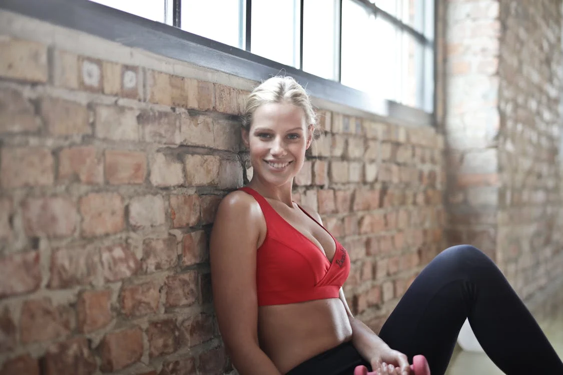 Foto di una donna in tenuta sportiva seduta per terra sorridendo