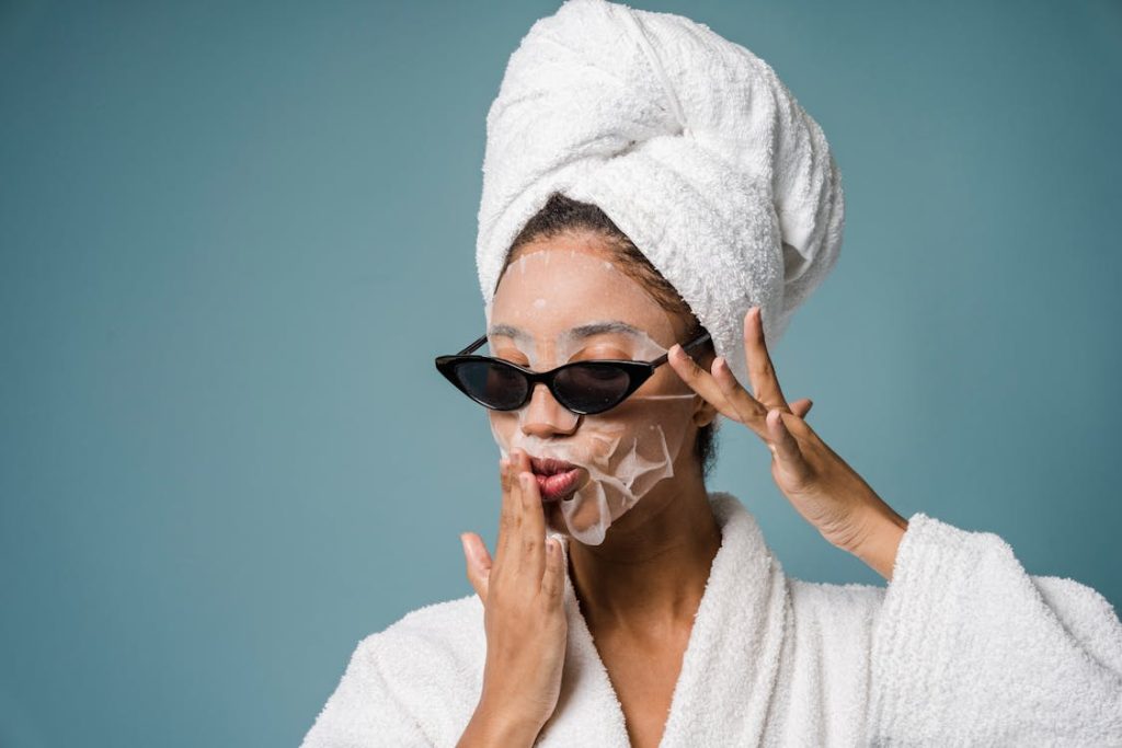 Foto di donna in accappatoio con l'asciugamano in testa, una maschera sul viso e gli occhiali da sole