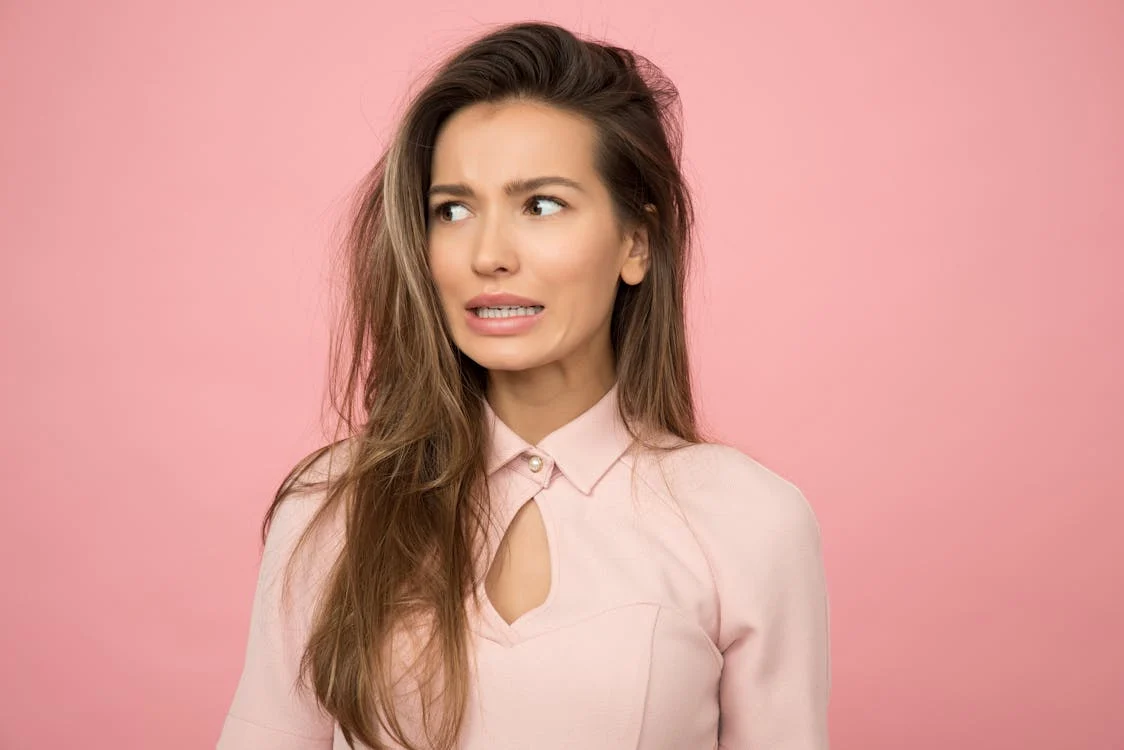 Foto di una ragazza che guarda da un lato con espressione preoccupata su sfondo rosa