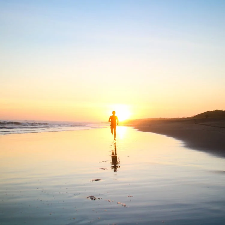 Foto di una persona in lontananza che sta correndo al tramonto in riva al mare