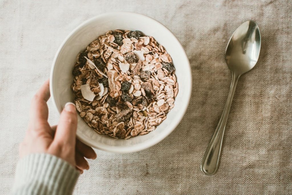 Foto di una tazza bianca di cereali con accanto un cucchiaio e una mano che la tiene