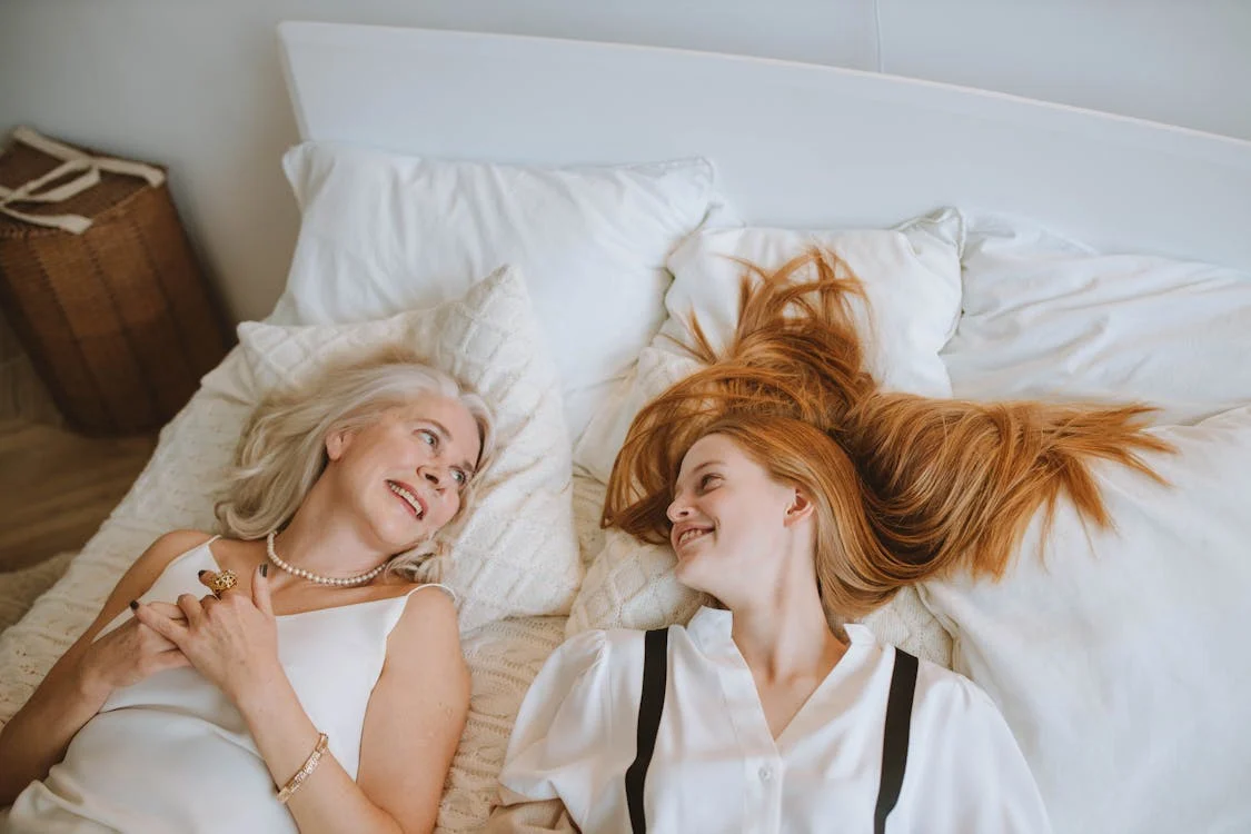 Foto di una donna matura e di una ragazza distese sul letto che si guardano e sorridono