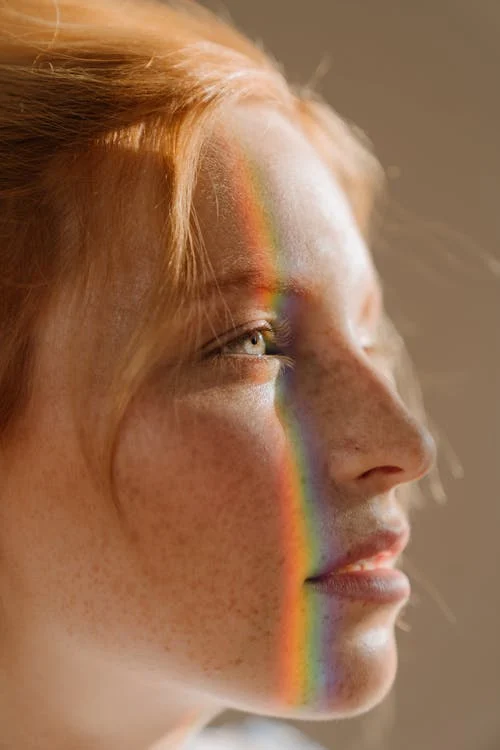 Foto del profilo di una ragazza con lentiggini e un arcobaleno riflesso