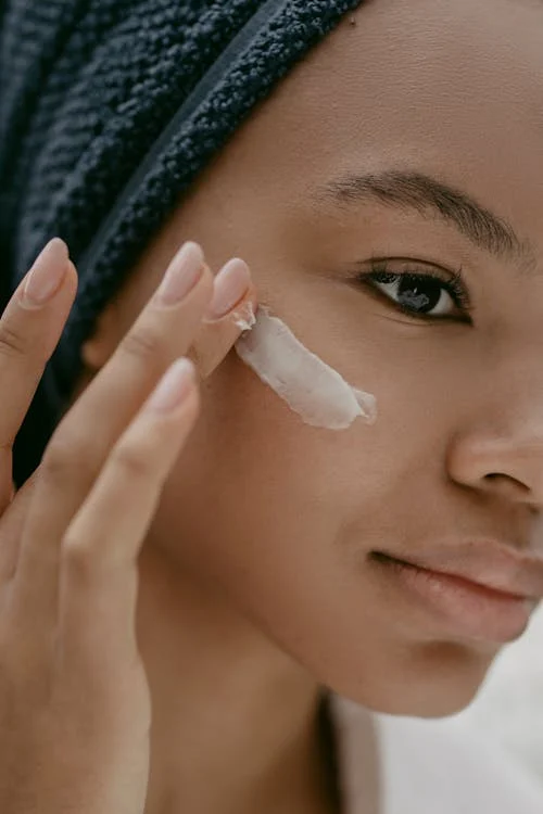 Foto del volto di una ragazza con la pelle scura mentre si spalma della crema