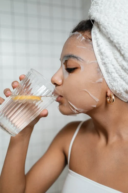 Foto di una donna con una maschera sul viso mentre beve acqua