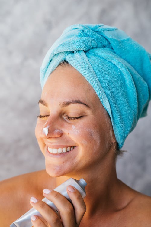 Foto di una donna che sorride e tiene in mano una crema che ha anche un po' sul viso