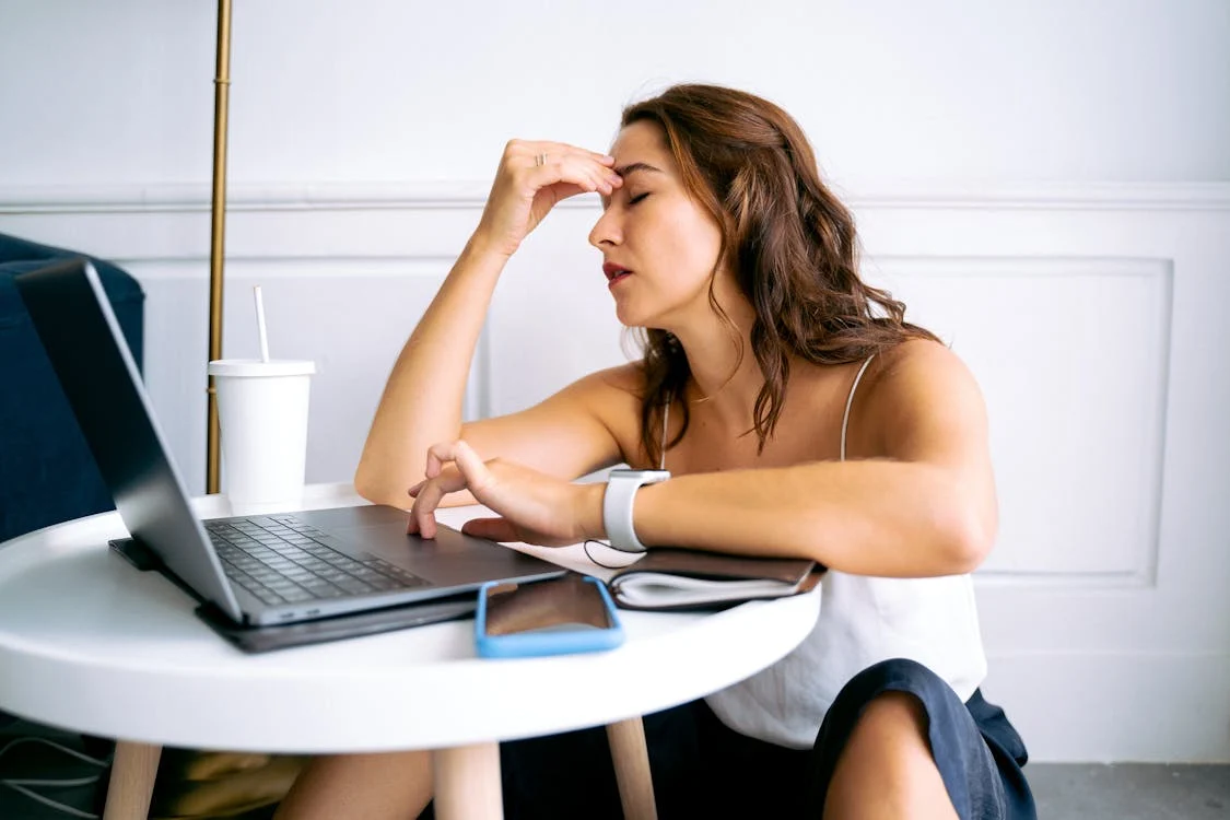 Foto di una donna seduta con una mano in fronte e gli occhi chiusi con davanti un pc 