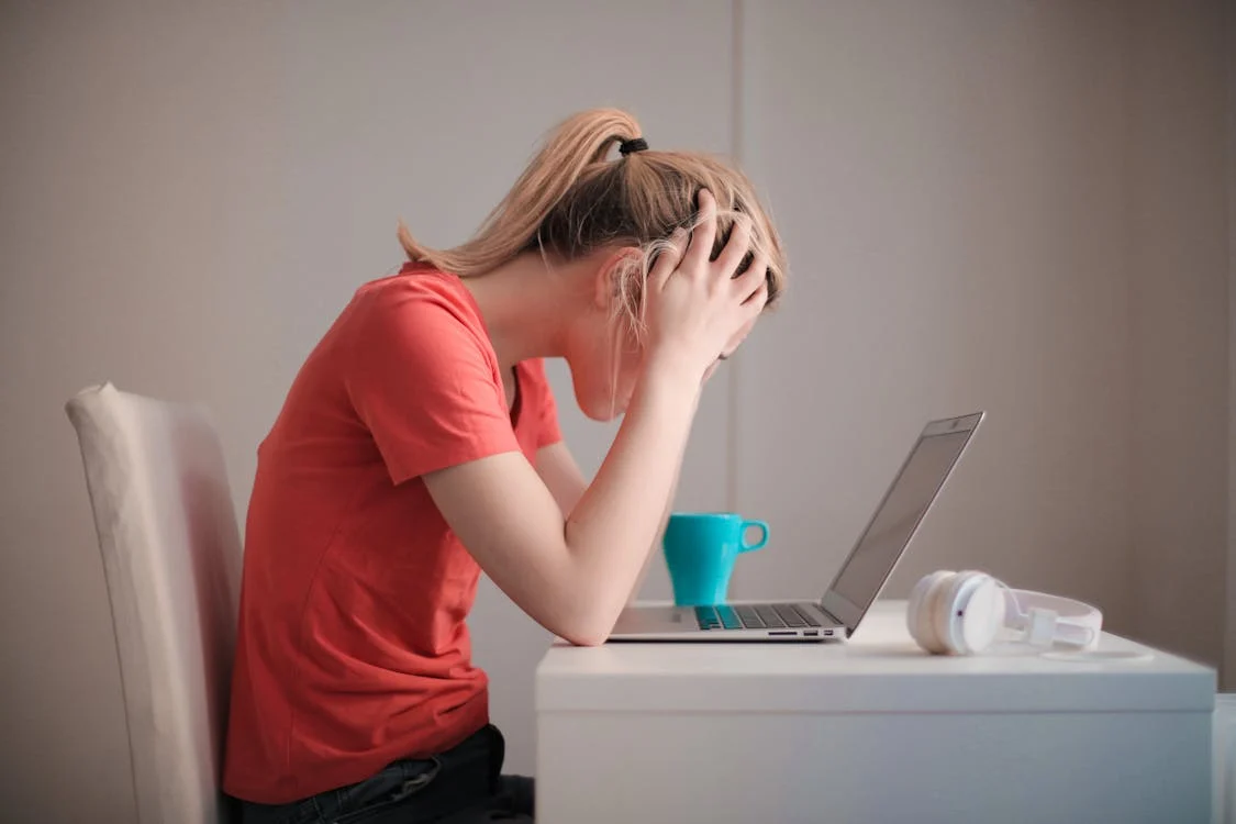 Foto di profilo di una ragazza seduta con la testa tra le mani e un computer davanti