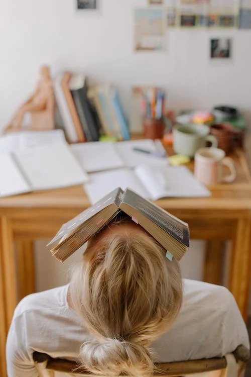 Foto di una donna con la testa poggiata indietro ed un libro in faccia