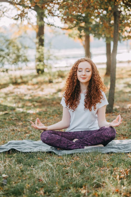 Foto di una ragazza in un parco seduta su un telo in posizione yoga