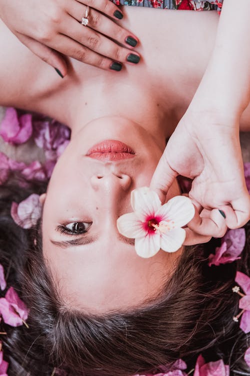 Foto di una ragazza distesa con dei petali intorno ed un fiore su un occhio