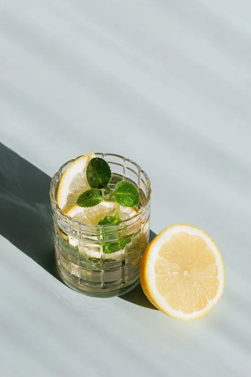 Foto di un bicchiere con dell'acqua, del limone dentro e una fogliolina verde e accanto al bicchiere metà limone 