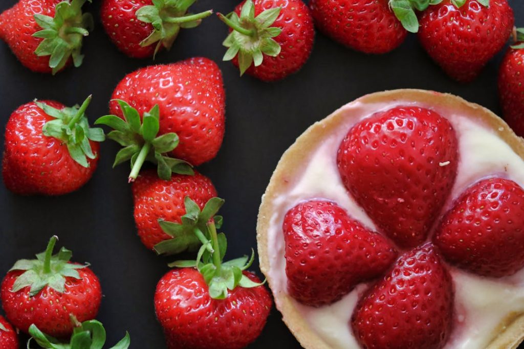 Foto di fragole intere e vicino un tortino con delle fragole tagliate a metà
