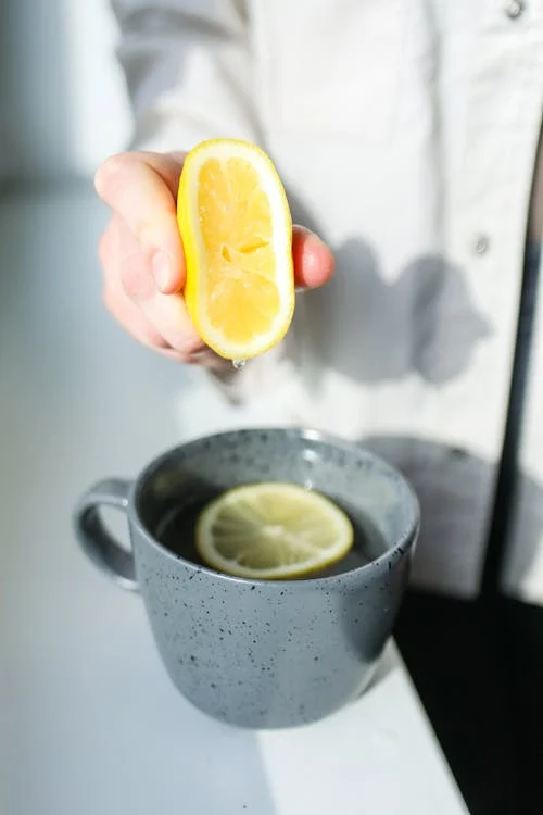 Foto di una tazza contenente una tisana dentro, una fetta di limone e una mano che sta spremendo del succo di limone all'interno