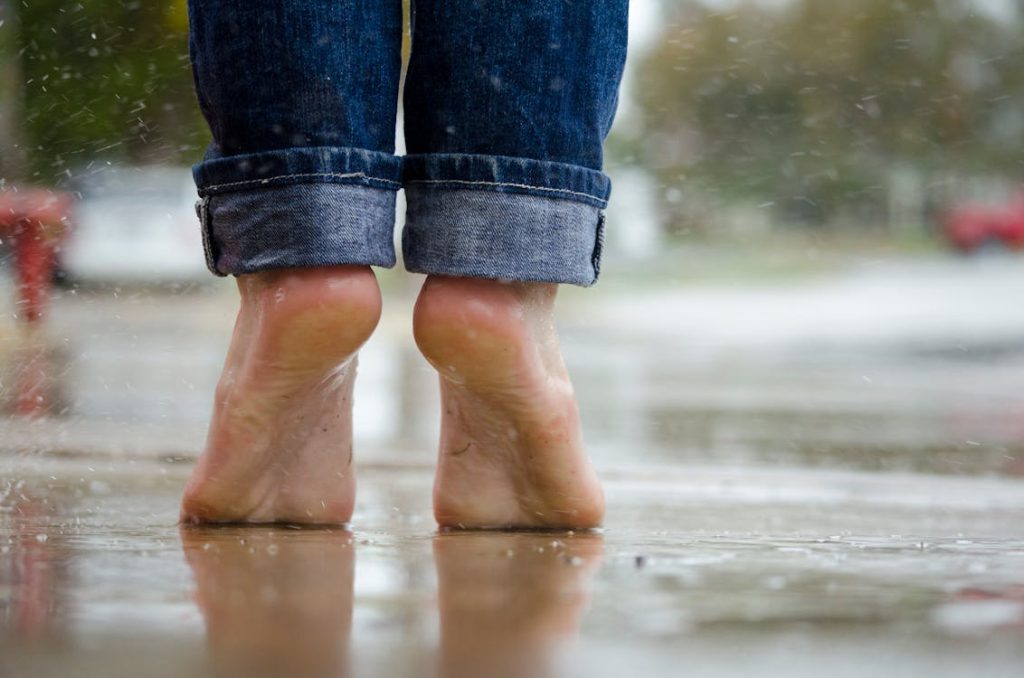 Foto di piedi presi da dietro di una persona che sta sulle punte a piedi scalzi sull'asfalto